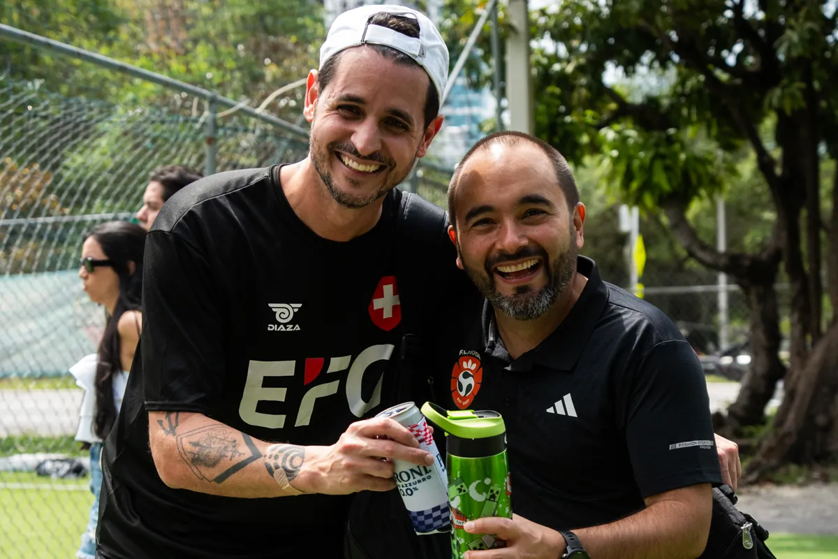 Two smiling men toasting at a CFL match day in Miami, one wearing the FCnoise crest